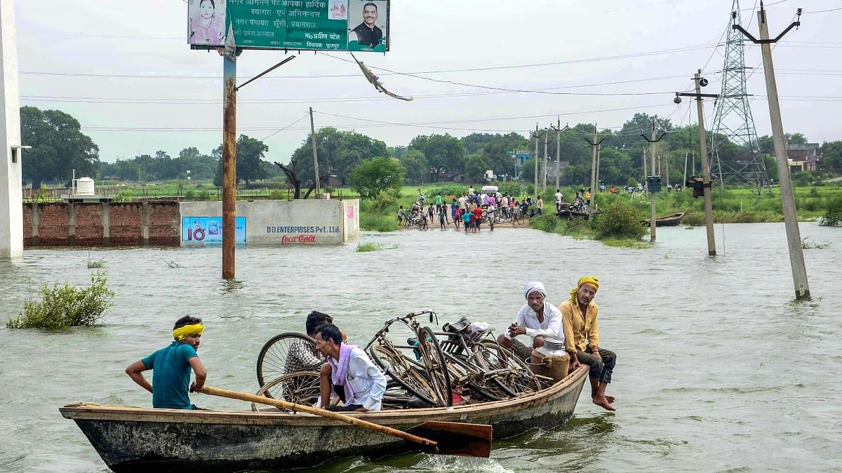 Villagers use a boat to commute at a flooded area after a rise in the water level of the Yamuna river following monsoon rains, in Prayagraj. Credit: PTI Photo