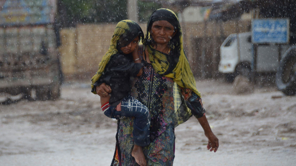 A woman carrying a child walks along a street during a heavy rainfall in the flood hit Dera Allah Yar town in Jaffarabad district, Balochistan province, on August 30, 2022. Credit: AFP Photo