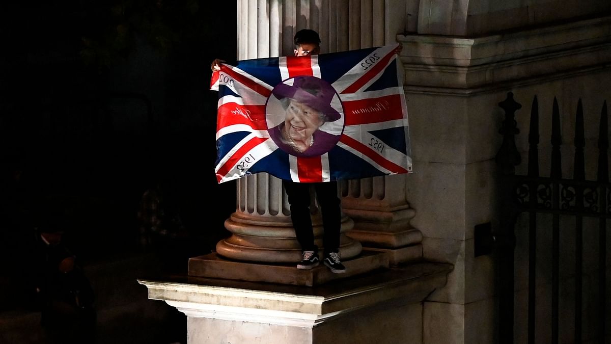 A local holding a Union Jack flag and stands on a corner of Marble Arch as he waits to see the coffin of Queen Elizabeth II in the royal hearse driving towards Buckingham Palace, in London. Credit: AFP Photo