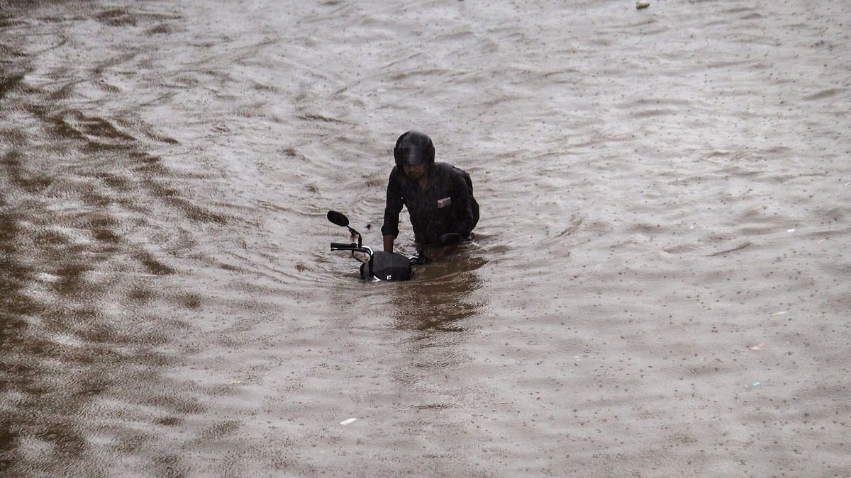 A biker pushes his two-wheeler as he wades through the waterlogged Delhi-Gurugram Expressway service road after heavy rainfall. Credit: PTI Photo