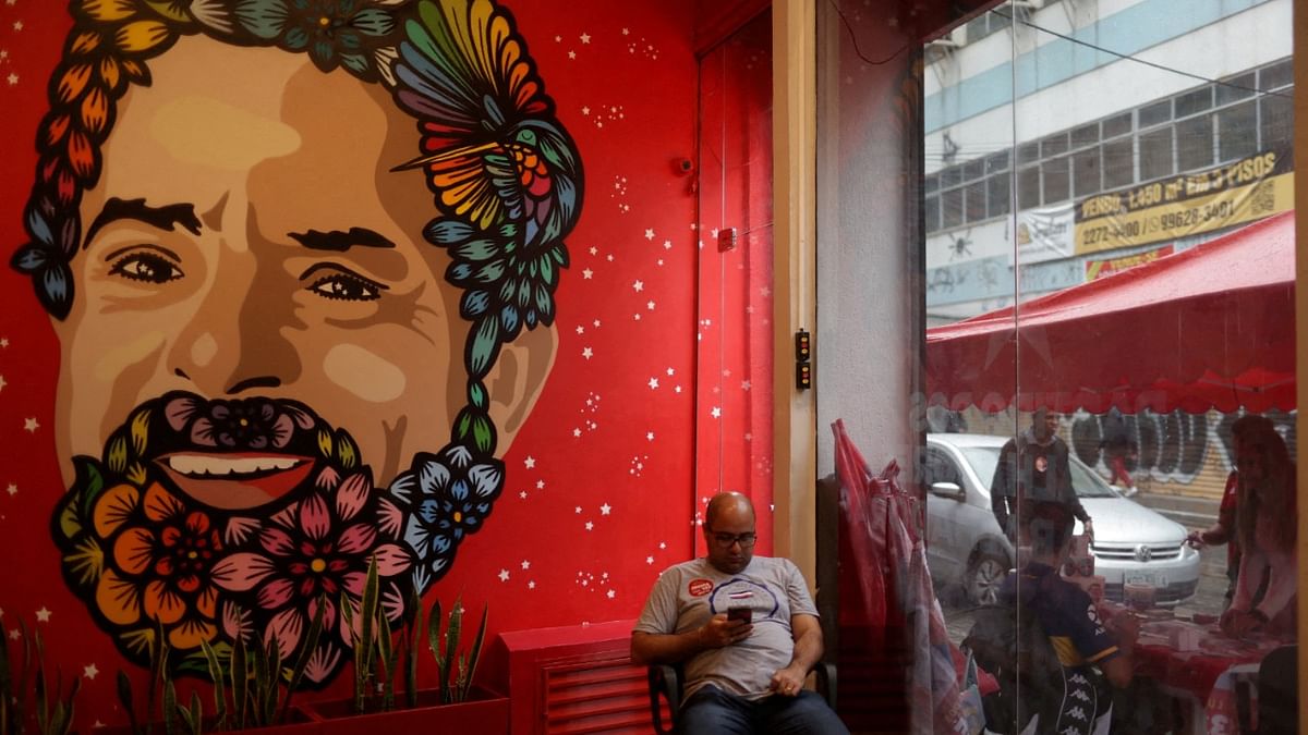 A man sits next to a graffiti of former Brazil's President and candidate for presidential election Luiz Inacio Lula da Silva at his campaign headquarters in Rio de Janeiro, Brazil. Credit: Reuters photo