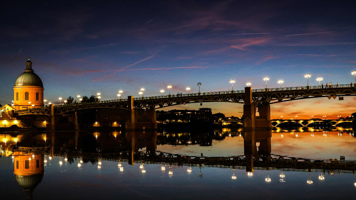 This photograph taken at dusk on October 3, 2022, shows the Saint-Pierre bridge on the Garonne river and the landmark Dome de La Grave (L) in Toulouse, southern France. Credit: AFP Photo