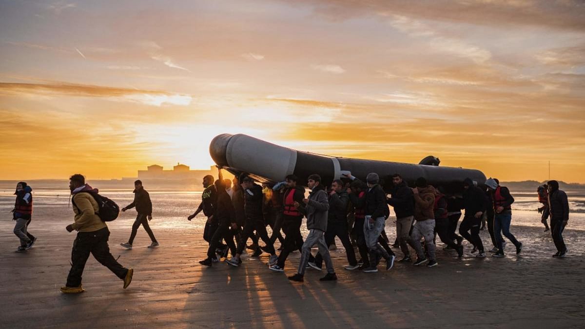Migrants carry a smuggling boat on their shoulders as they prepare to embark on the beach of Gravelines, near Dunkirk, northern France on October 12, 2022, in a attempt to cross the English Channel. Credit: AFP Photo