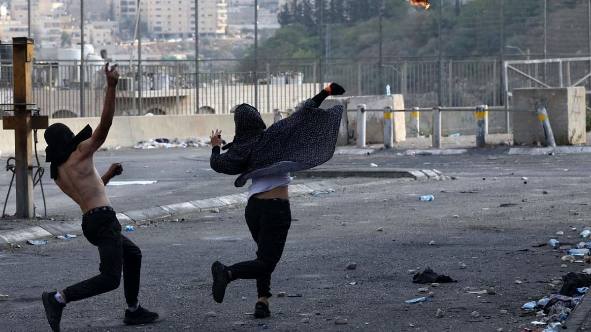 A Palestinian woman throws a Molotiv cocktail towards Israeli security forces as another hurls rocks, during confrontations with them in the Shuafat refugee camp in Israeli-annexed east Jerusalem, on October 12, 2022. Credit: AFP Photo