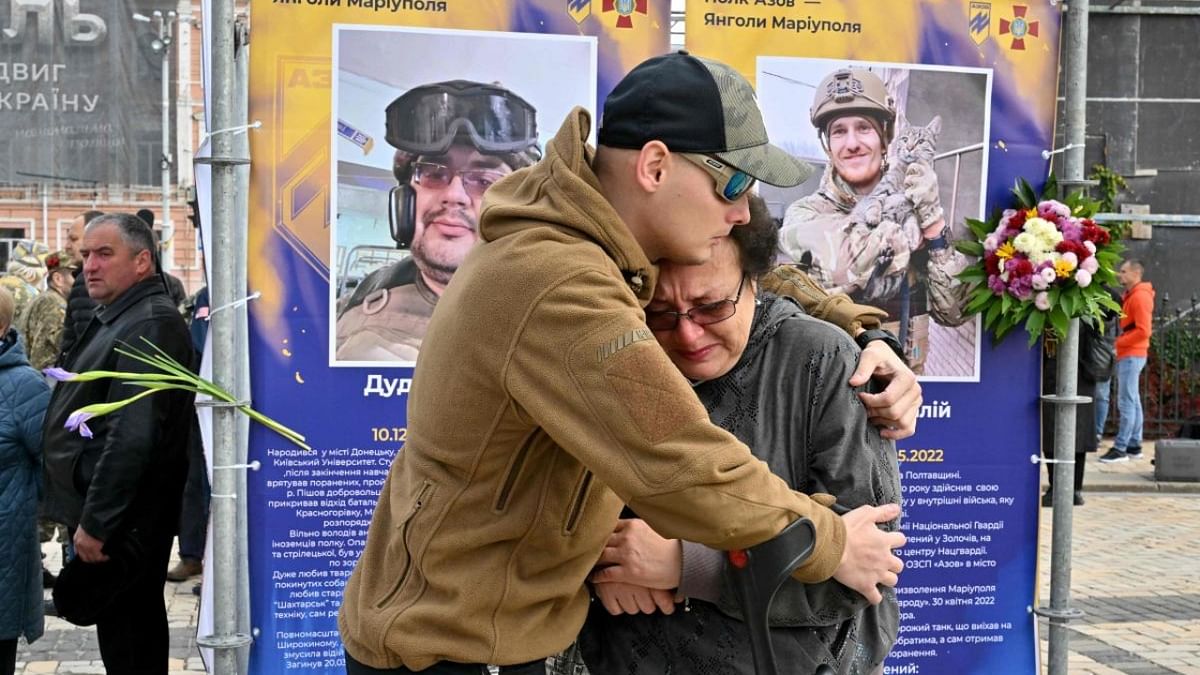 A young man hugs a woman as she cries at the portraits of two dead servicemen during the opening of an open-air exhibition