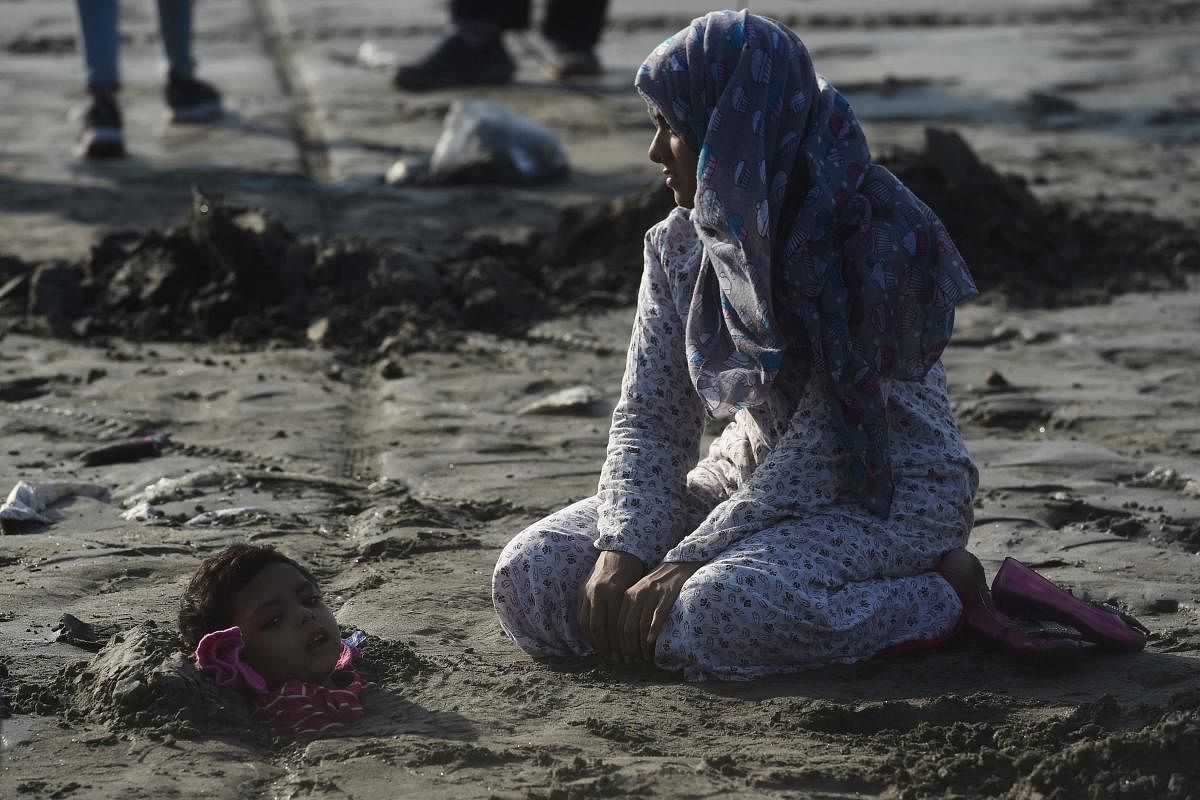 A relative sits next to a child covered with sand in a beach with the believe that exposure during a solar eclipse will heal an illness, in Karachi. Credit: AFP Photo