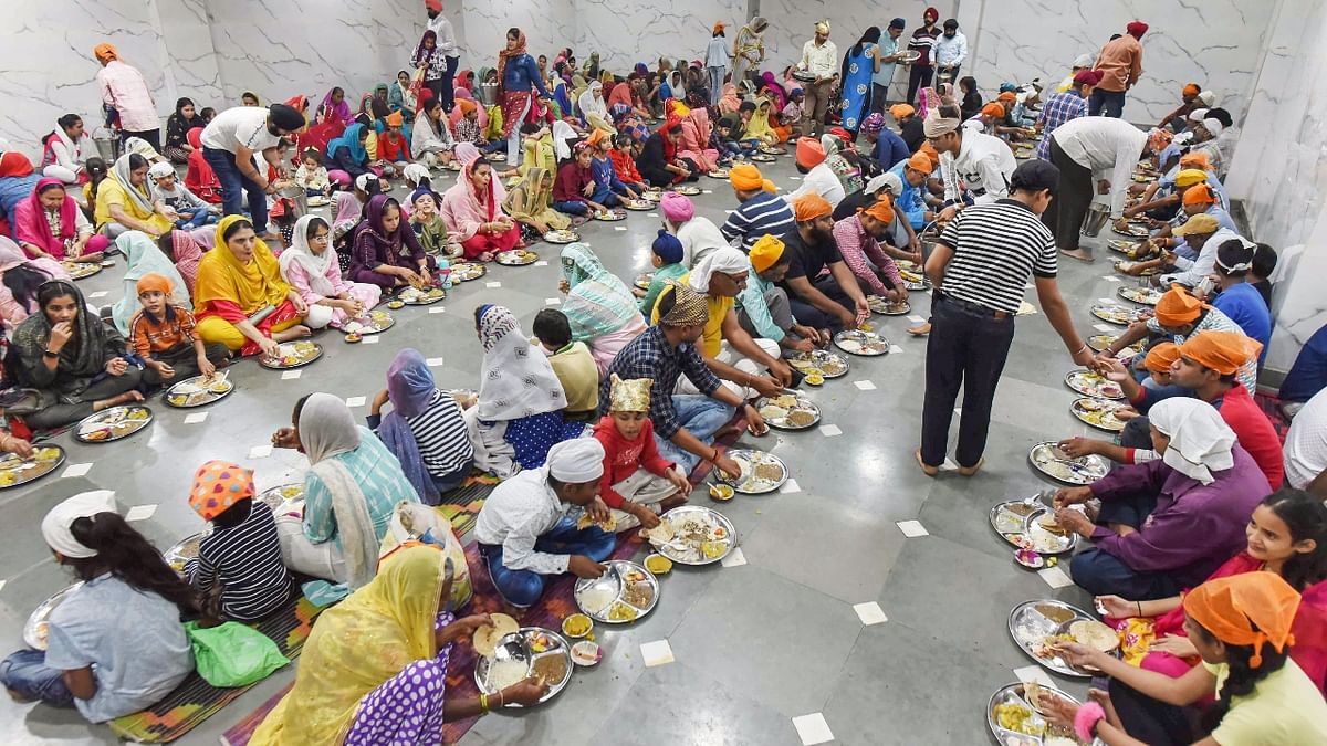 Devotees eat 'langar' during the birth anniversary celebrations of Guru Nanak Dev, at a gurudwara in Prayagraj. Credit: PTI Photo