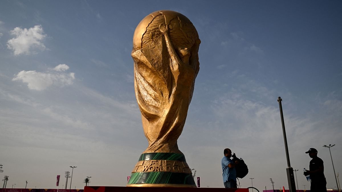 Men walk past a FIFA World Cup trophy replica outside the Ahmed bin Ali Stadium in Al-Rayyan on November 12, 2022, ahead of the Qatar 2022 FIFA World Cup football tournament. Credit: AFP Photo