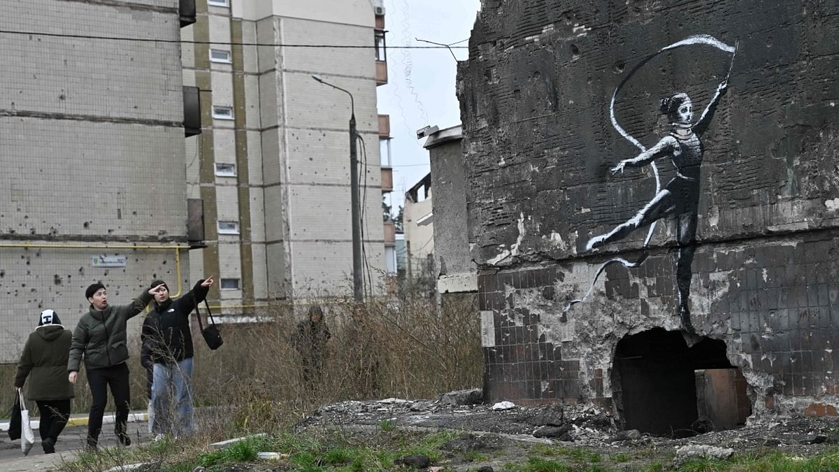 Local residents look at a Banksy-style graffiti on the wall of a destroyed residential building, but its origin remains unconfirmed by the artist, in Irpin, near Kyiv on November 12, 2022. Credit: AFP Photo
