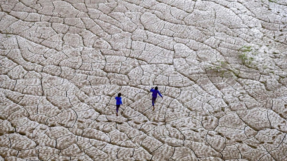 Boys run along the dried-up portion of a riverbed on the banks of river Ganges in Prayagraj. Credit: AFP Photo