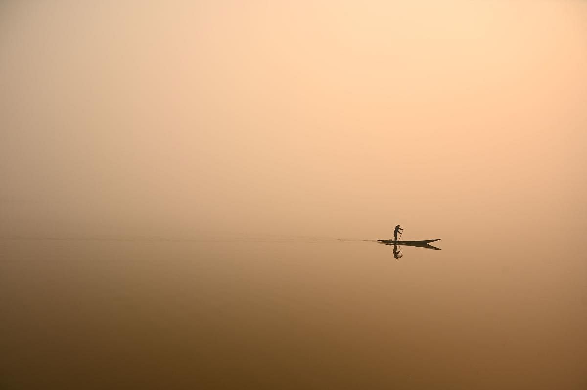 A man steers a boat in Dal Lake amid a thick blanket of fog in Srinagar. Credit: AFP Photo