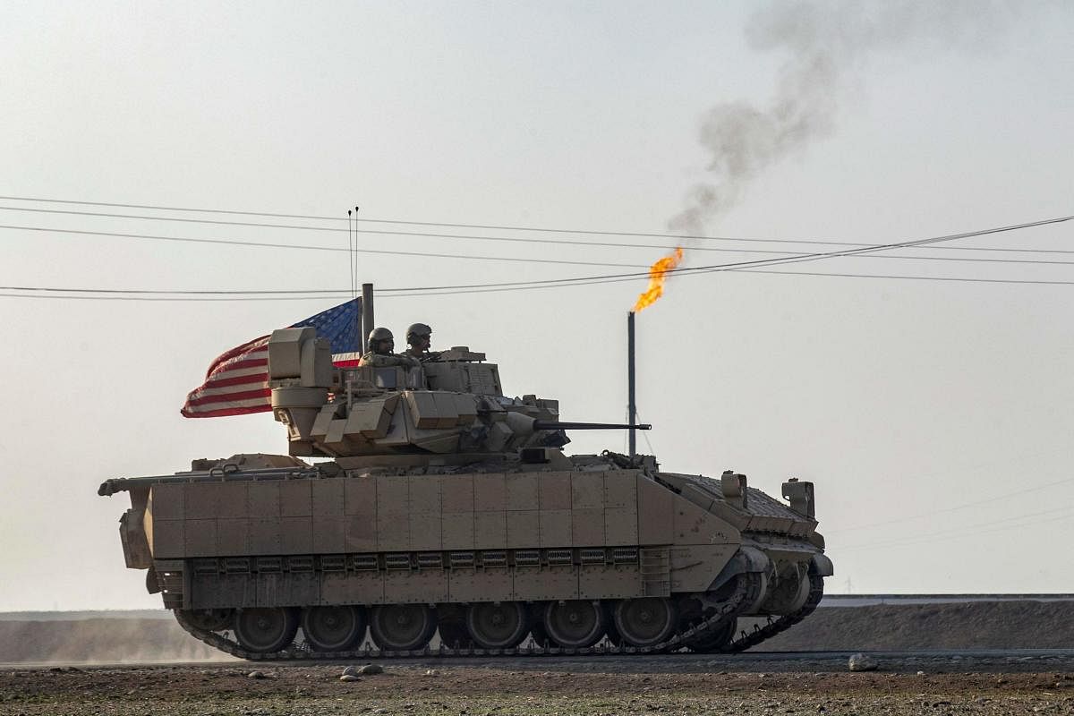 US soldiers in a Bradley Fighting Vehicle (BFV) drive past a flare stack near a local oil field as they patrol the countryside of Rumaylan (Rmeilan) in Syria's northeastern Hasakeh province, near the border with Turkey. Credit: AFP Photo