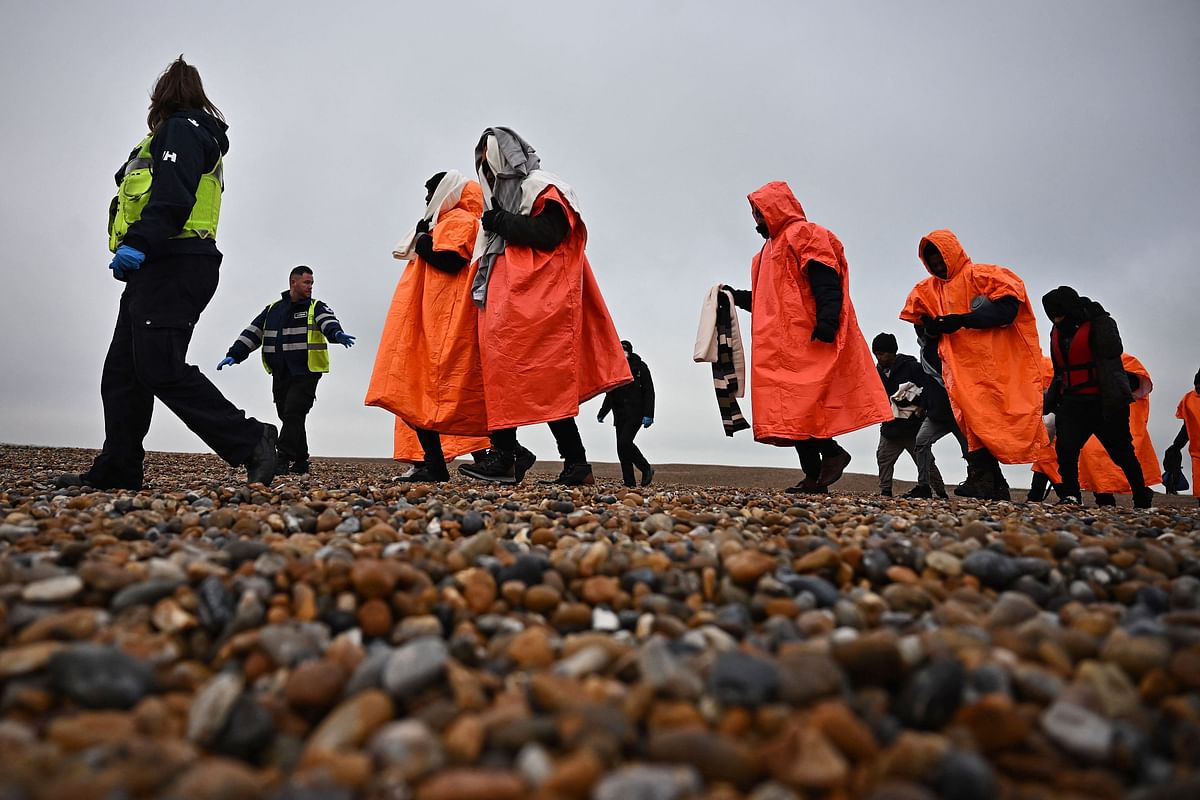 A British Immigration Enforcement officer (L) and an Interforce security officer (2L), escort migrants, picked up at sea by an Royal National Lifeboat Institution (RNLI) lifeboat whilst they were attempting to cross the English Channel, on the shore at Dungeness on the southeast coast of England. Credit: AFP Photo