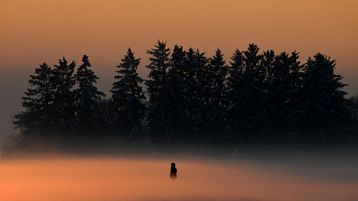 A stroller enjoys the sunset near Puchheim village in southern Germany, on a foggy December 17, 2022 with temperatures around minus five degrees Celsius. Credit: AFP Photo