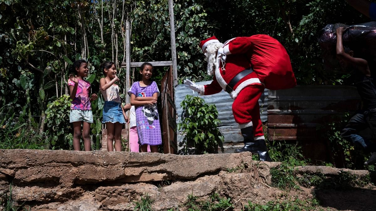 A man dressed as Santa Claus carrying his bag with gifts greets children in the Barrio Nuevo community during an unusual walk up a hill between graves to visit children and distribute toys in poor areas in Caracas, on December 17, 2022. Credit: AFP Photo