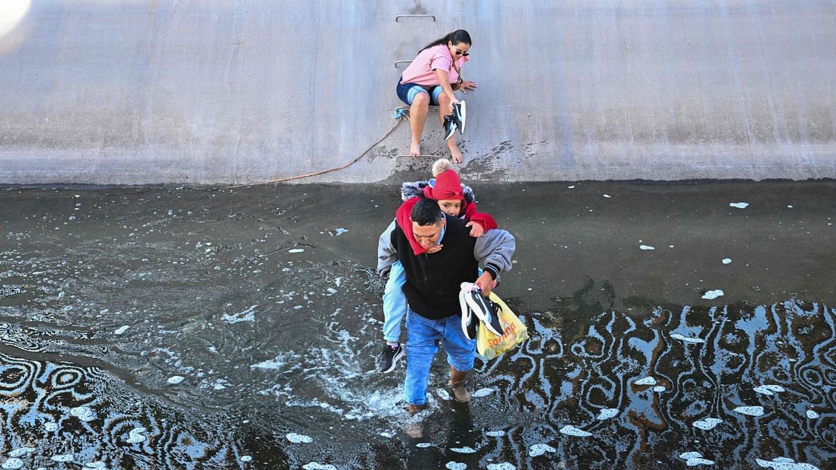 A family of migrants from Columbia makes their way through a water canal after crossing under a hole in the US-Mexico border wall in El Paso, Texas, on December 19, 2022. Credit: AFP Photo