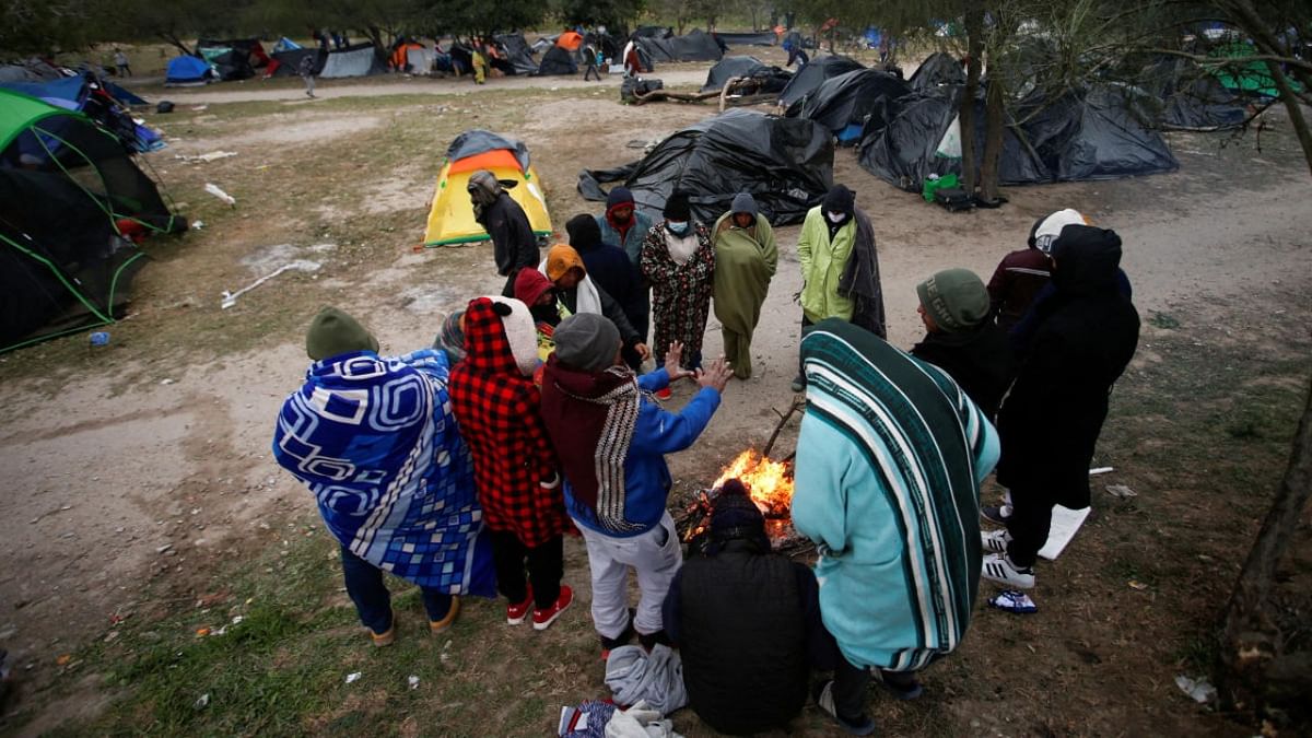Asylum-seeking migrants gather around a fire to warm up during a day of high winds and low temperatures at a makeshift encampment near the border between the US and Mexico. Credit: Reuters photo