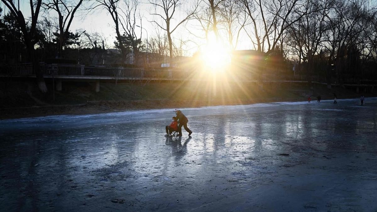 A man pushes a child on a sled on a frozen river in Beijing on December 27, 2022. Credit: AFP Photo