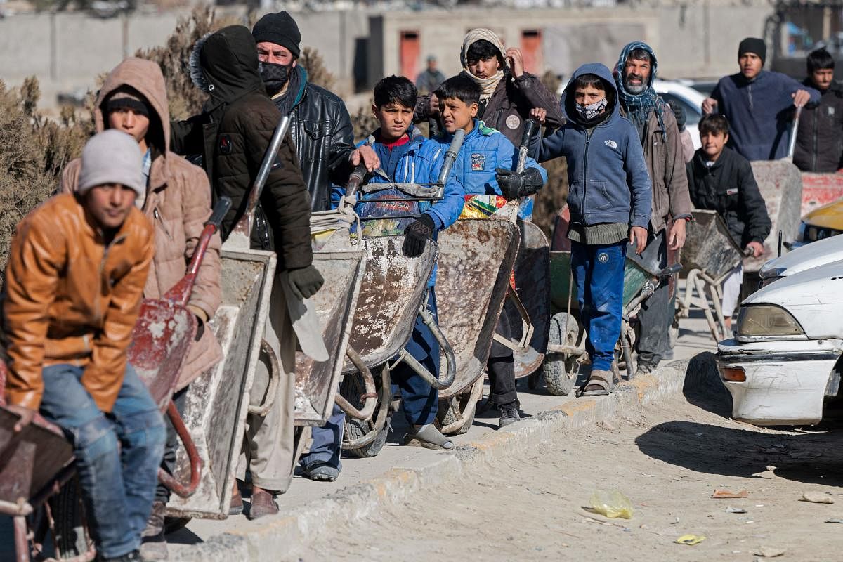 Afghan boys with their wheelbarrows stand in a queue as they wait to receive food aid from a non-governmental organisation (NGO) in Kabul. - Aid groups say they have been