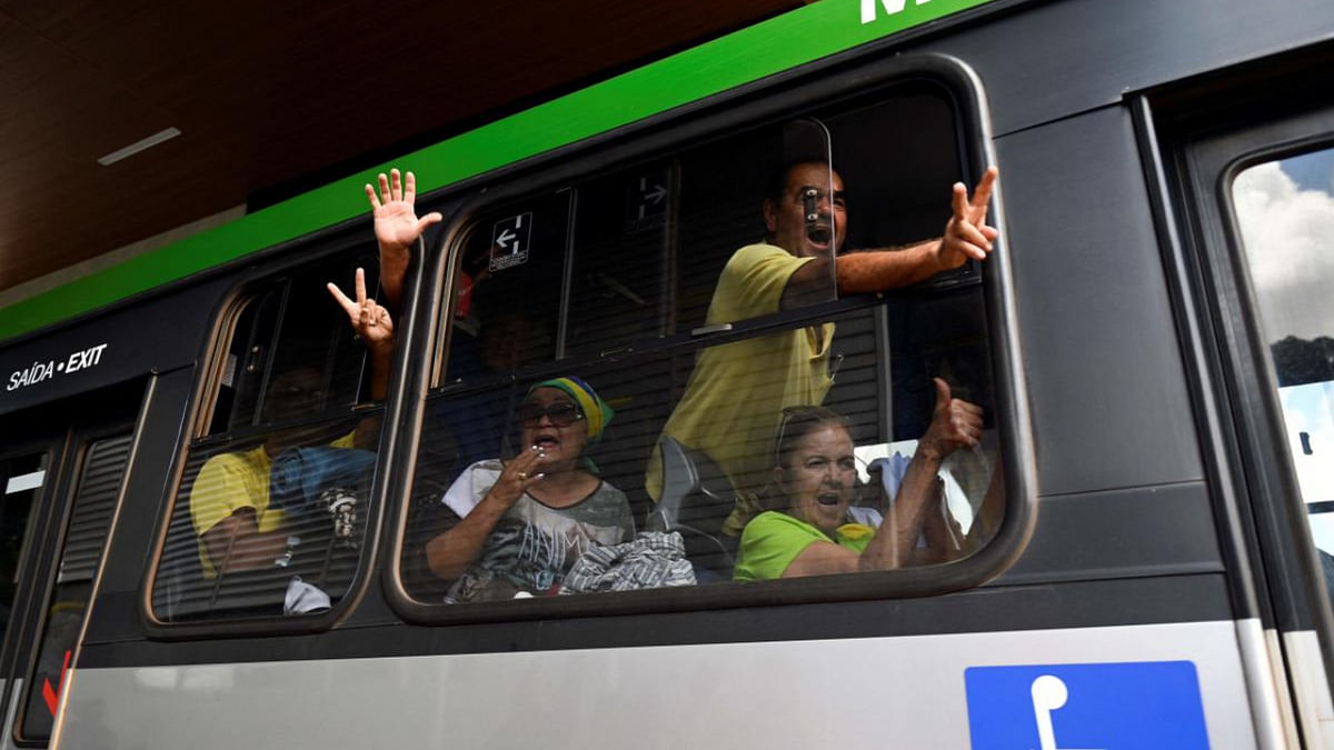 A small group of supporters of Brazil's far-right ex-president Jair Bolsonaro who had been arrested after they invaded the Congress, presidential palace and Supreme Court, gesture from inside a bus while leaving the Federal Police headquarters in Brasilia. Credit: AFP Photo