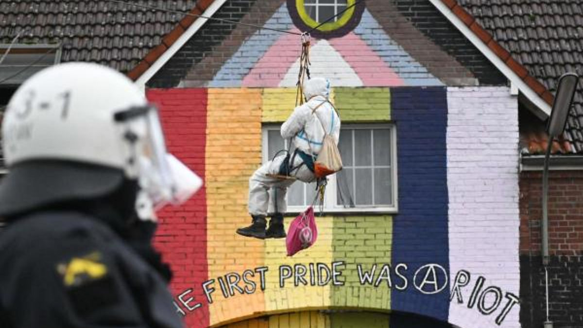 A policeman looks on as an activist hangs on a rope over a house while the lettering on the facade reads 'The first pride was a riot' in the village of Luetzerath, western Germany. Credit: AFP Photo