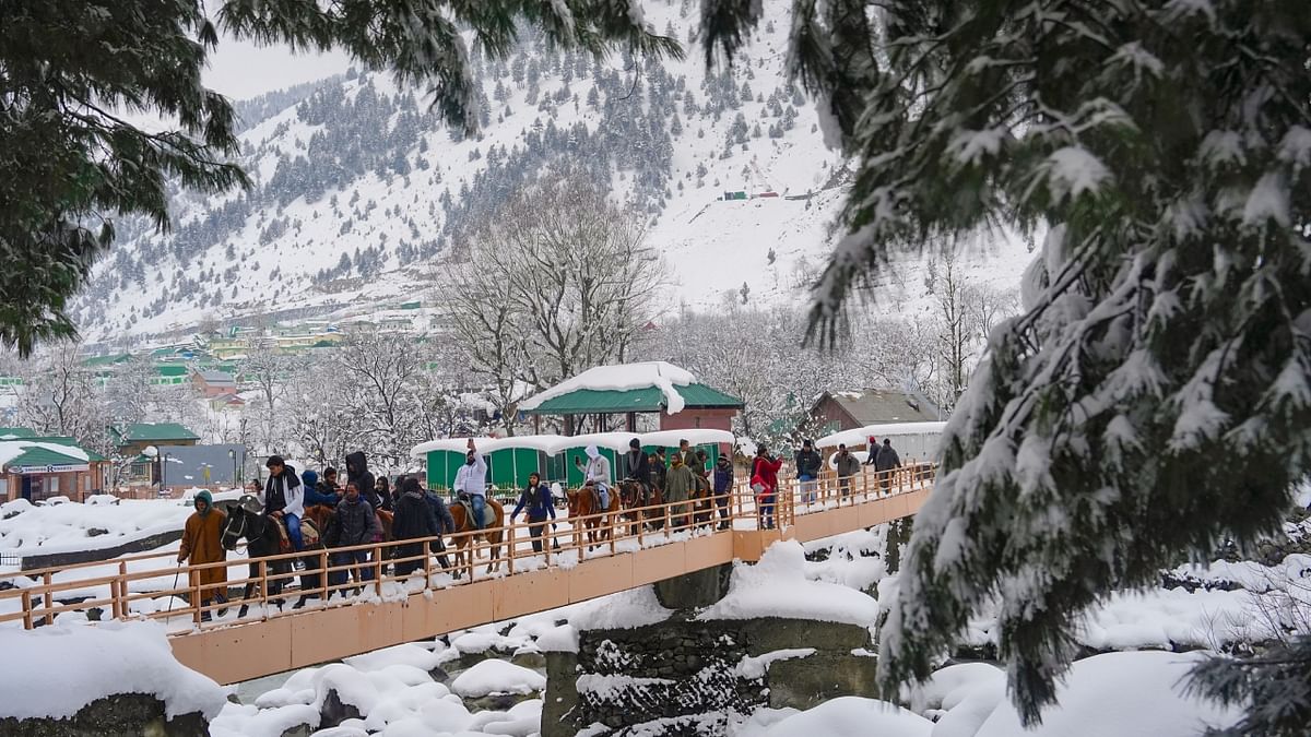 Tourists cross a bridge after fresh snowfall at Sonamarg in Ganderbal district of Kashmir. Credit; PTI Photo