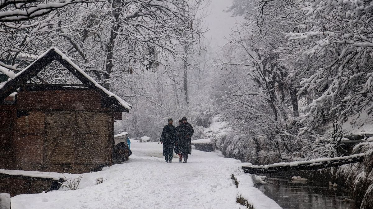 People walk on a snow-covered road during fresh snowfall in Tangmarg area of North Kashmir. Credit: PTI Photo