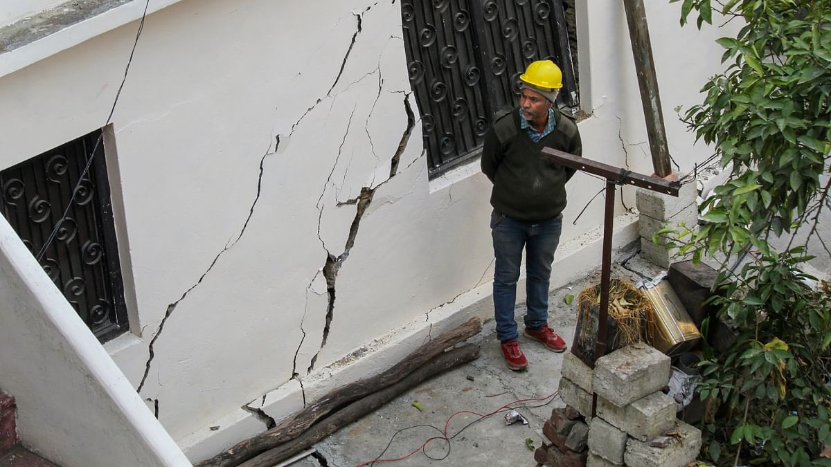 A worker looks at cracks that appeared in a building, at the land subsidence affected area in Joshimath. Credit: PTI Photo