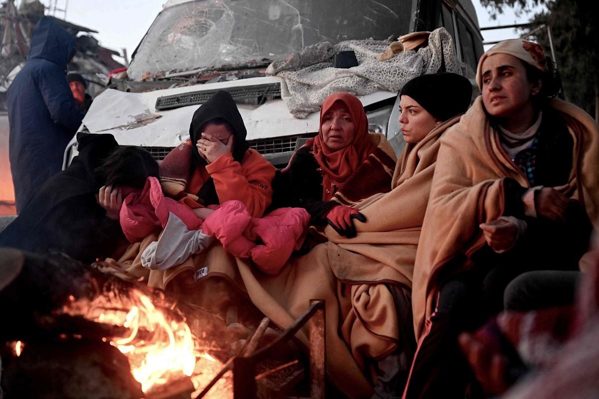 People sit near a bonfire amidst the rubble of collapsed buildings in Kahramanmaras, on February 8, 2023, two days after a 7,8-magnitude earthquake struck southeast Turkey. - Searchers were still pulling survivors on February 8 from the rubble of the earthquake that killed over 11,200 people in Turkey and Syria, even as the window for rescues narrowed. Credit: AFP Photo
