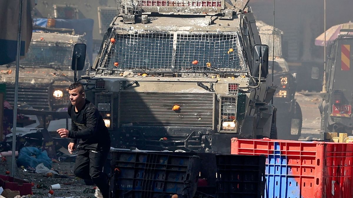 A Palestinian runs for cover from an Israeli military vehicle during a raid in the occupied West Bank city of Nablus, on February 22, 2023. Credit: AFP Photo