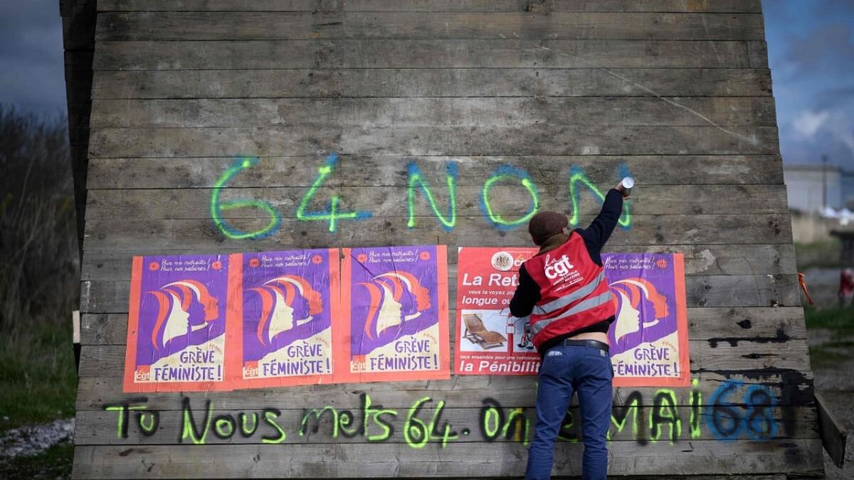 A nnionists of the French union General Confederation of Labour (CGT) uses a spray can to write '64-no' on a barrier, part of the roadblock to the the oil terminals at the Total Energies refinery during a protest against the government's proposed pensions overhaul in Donges. Credit: AFP Photo