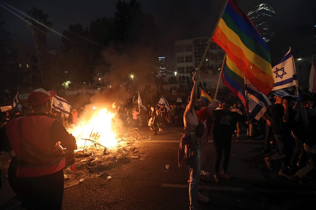 Protesters block a road and hold national and rainbow flags as they gather around a bonfire during a rally against the Israeli government's judicial reform in Tel Aviv. Credit: AFP Photo