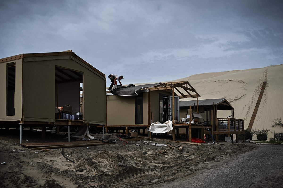 This photograph taken on March 29, 2023 shows workers (top R) installing stairs on the Pyla sand dune while another covers the roof of a bungalow during the rebuilding and preparation work at the