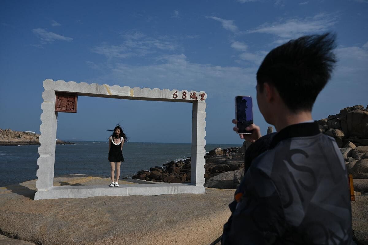 A man takes a photo of a woman under a frame in front of the Taiwan Strait which marks the closest point in the mainland to Taiwan, on Pingtan island, in China's southeast Fujian province. Credit: AFP Photo