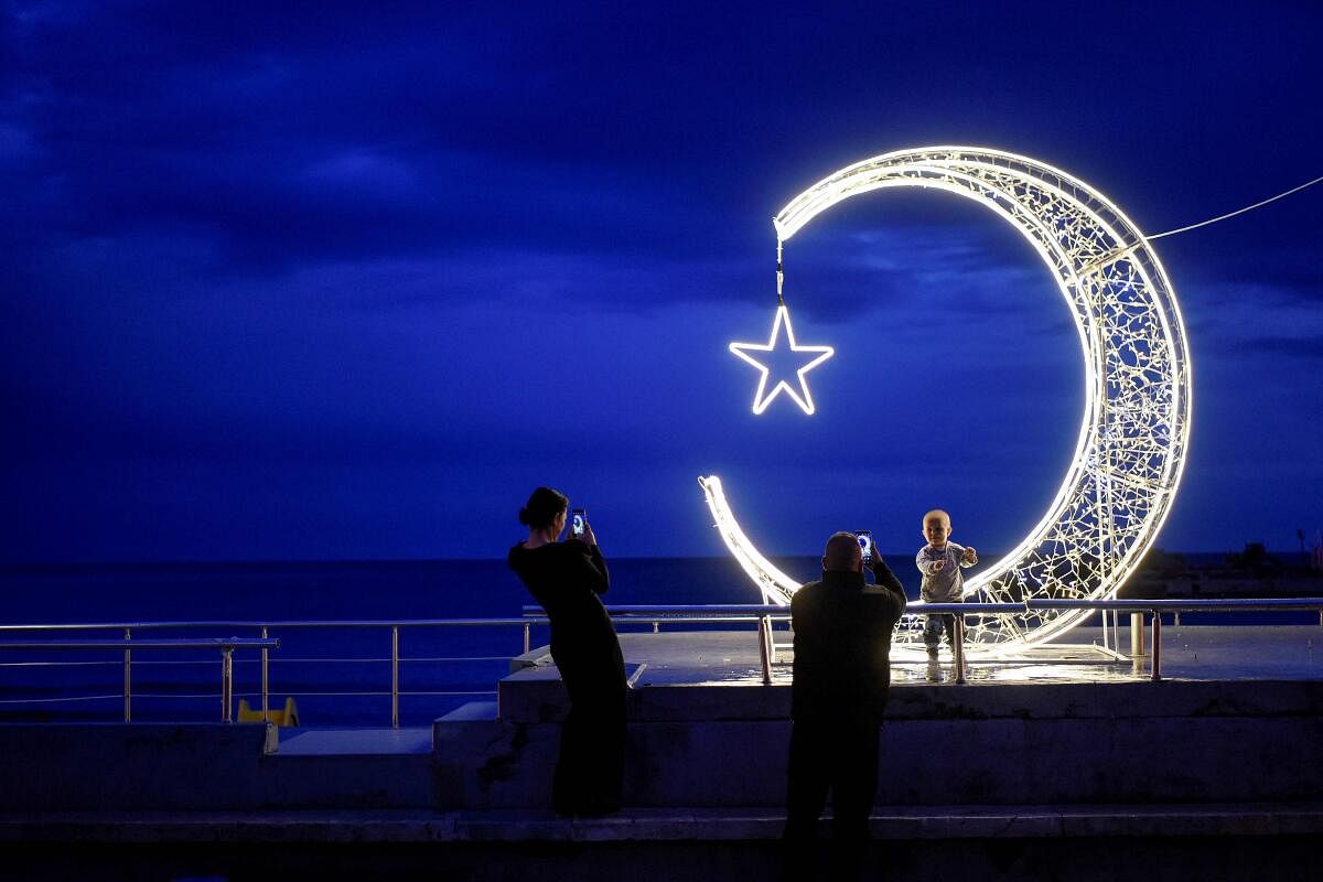 A man and his children stand in front of a crescent moon-shaped decoration placed in the town of Ulcinj. credit: AFP Photo