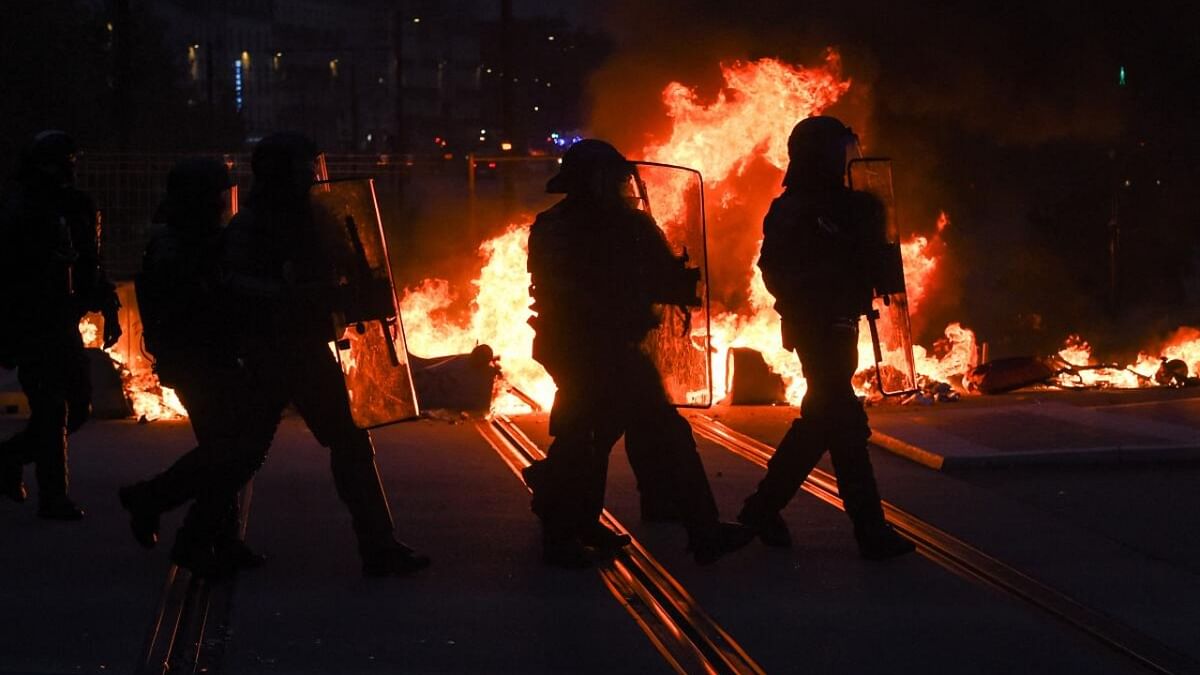 French anti-riot police officers walk in front of waste bins on fire during clashes with police on the sidelines of a demonstration after France's Constitutional Council approved the key elements of a pension reform, in Nantes, western France, on April 14, 2023. Credit: AFP Photo