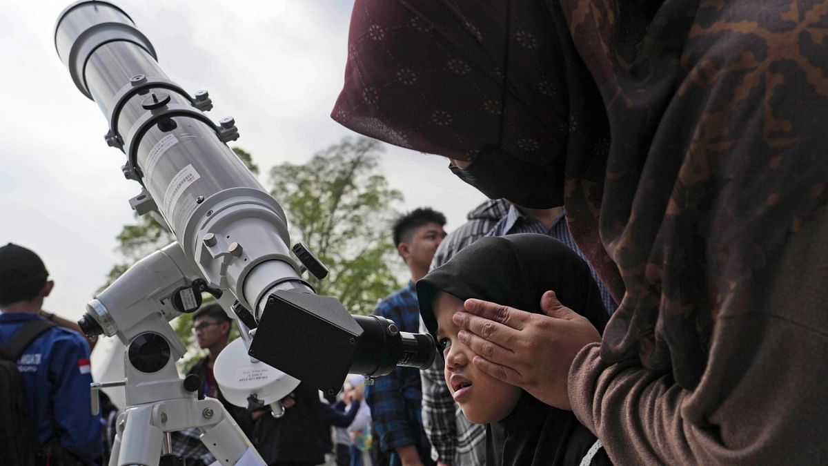 A woman assists her daughter as she looks through a telescope to watch the solar eclipse. Credit: AP Photo