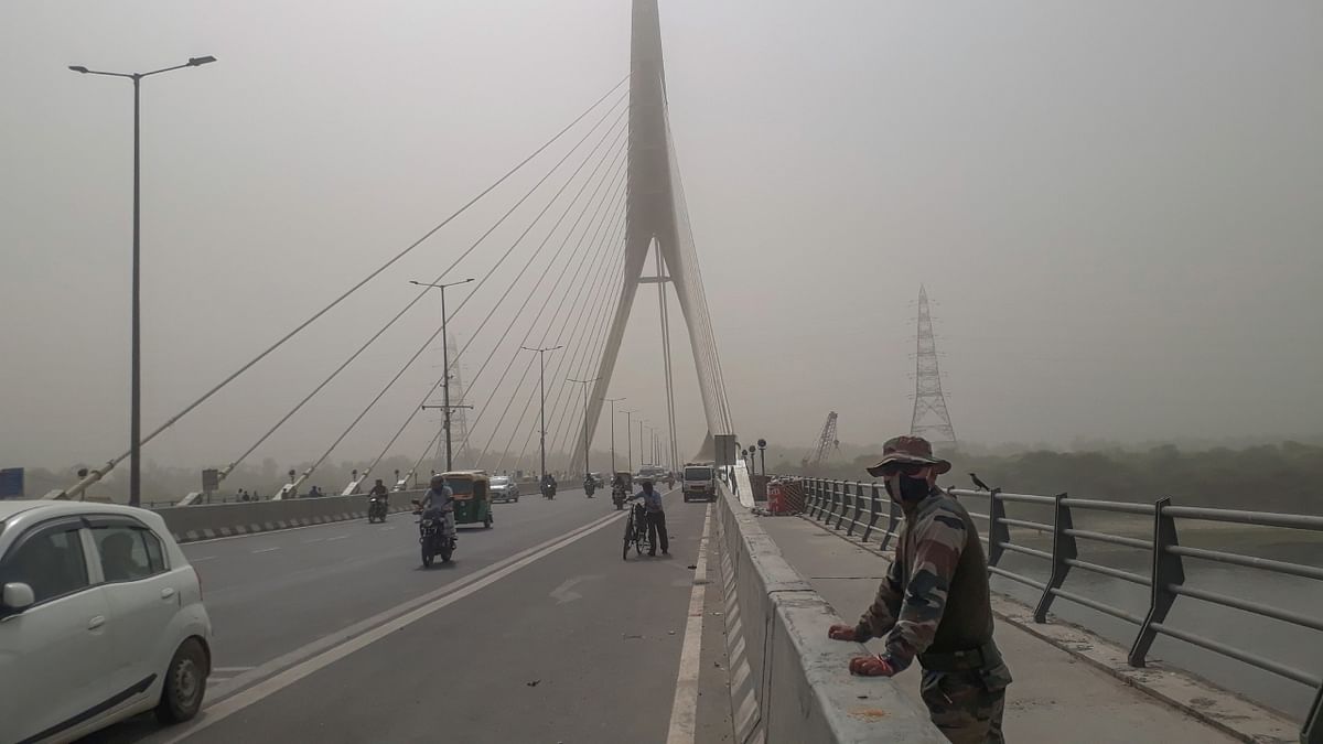 A security personnel protecting himself from dust by wearing a mask as he stands guard on the Signature Bridge, in New Delhi. Credit: PTI Photo