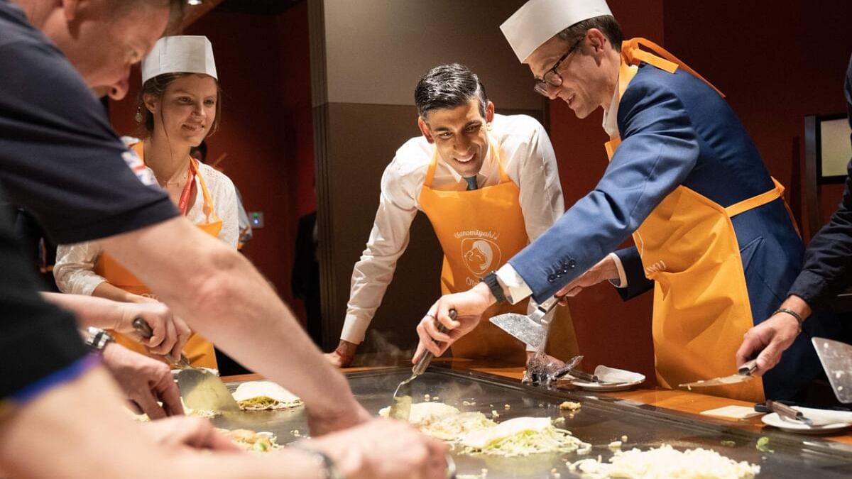 Britain's Prime Minister Rishi Sunak (2nd R) is shown how to make traditional Japanese Okonomiyaki pancakes at a restaurant in Hiroshima with travelling British journalists including BBC Political Editor, Chris Mason (R), on the sidelines of the G7 Summit Leaders' Meeting on May 20, 2023. Credit: AFP Photo