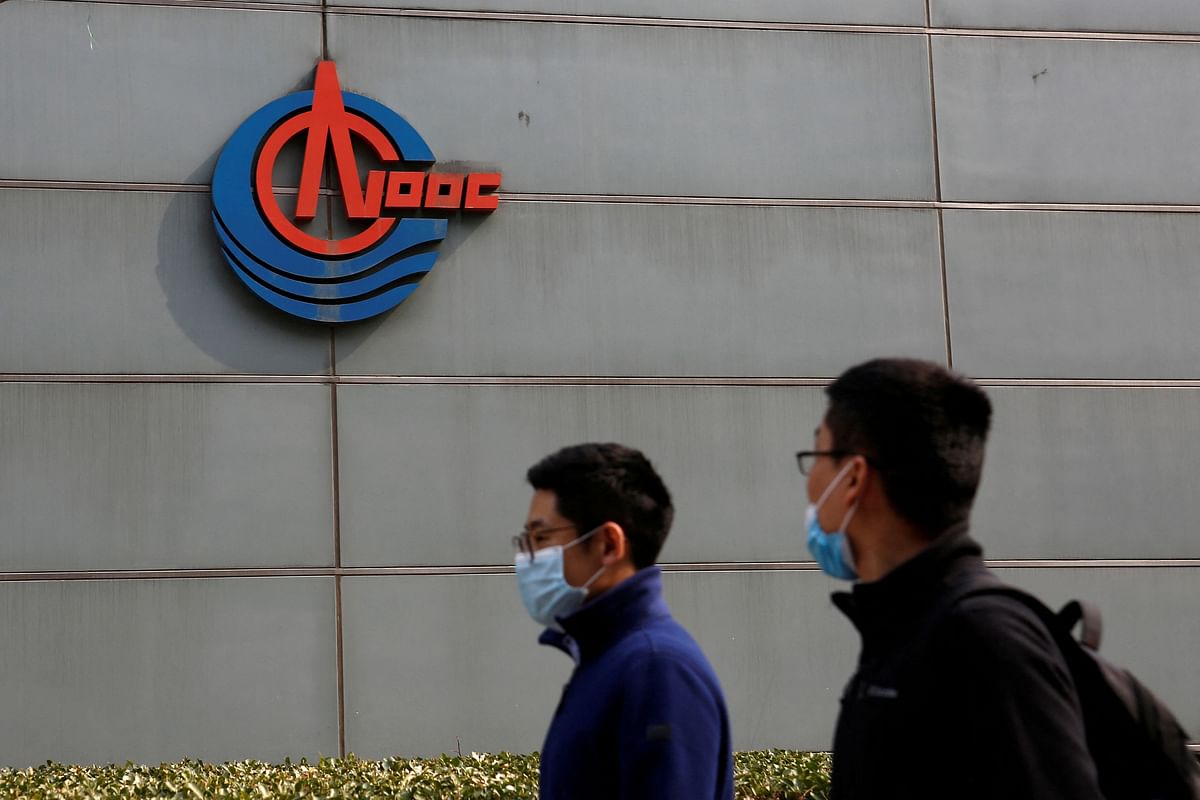 Men wearing face masks walk past a sign of China National Offshore Oil Corp (CNOOC) outside its headquarters in Beijing, China March 8, 2021. Credit: Reuters Photo