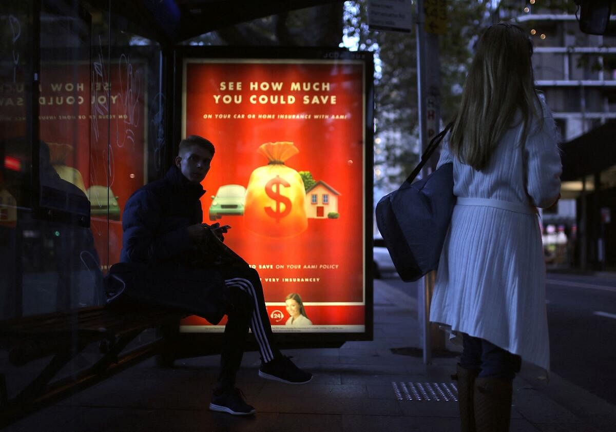 Members of the public wait at a bus stop as an illuminated financial advertisement adorns the bus shelter in central Sydney. Credit: Reuters Photo