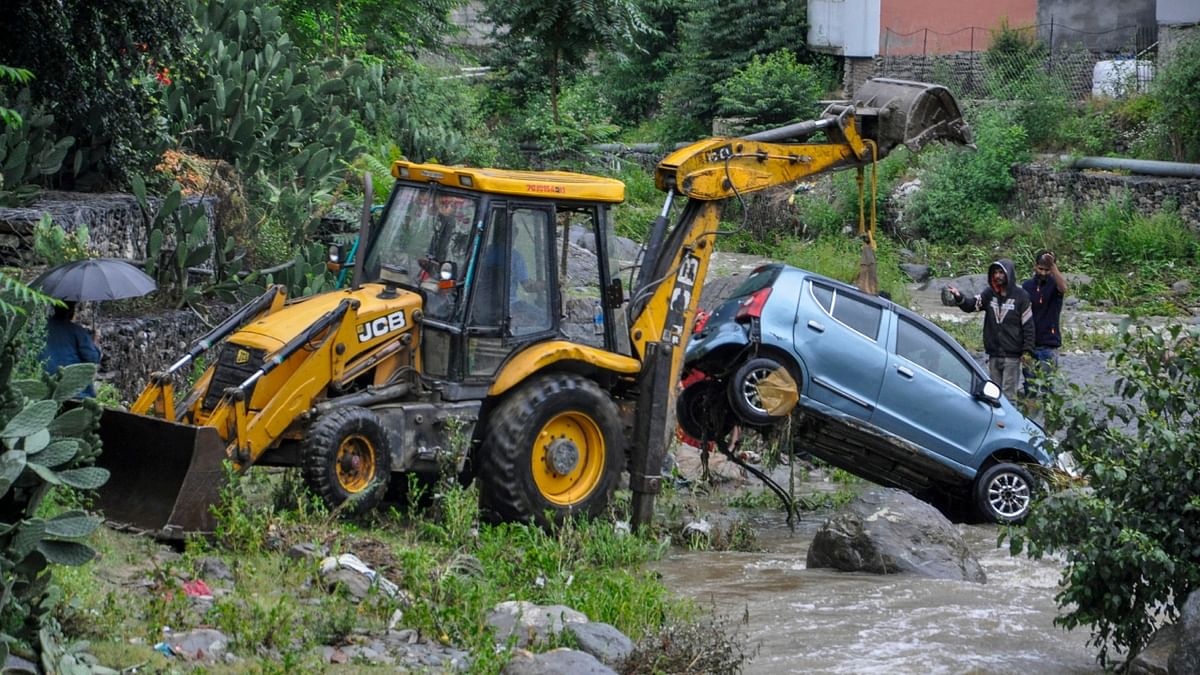 A craine lifts a car out of floodwater after it got swept away following heavy rainfall, in Kullu. Credit: PTI Photo