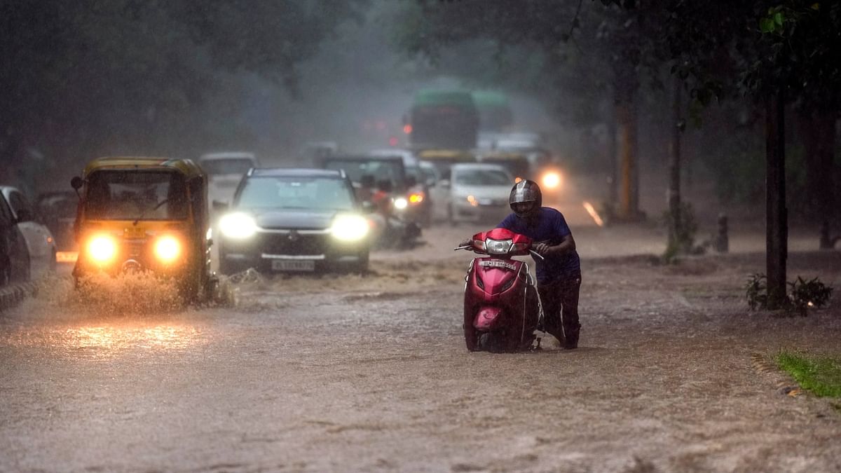 Commuters move through waterlogged Brigadier Hoshiyar Singh Marg near Sarojini Nagar during monsoon rain, in New Delhi. Credit: PTI Photo