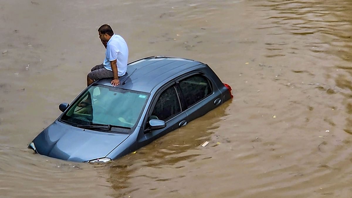 A commuter sits atop a car stuck on a waterlogged road at Subhash Chowk after monsoon rain, in Gurugram. Credit: PTI Photo