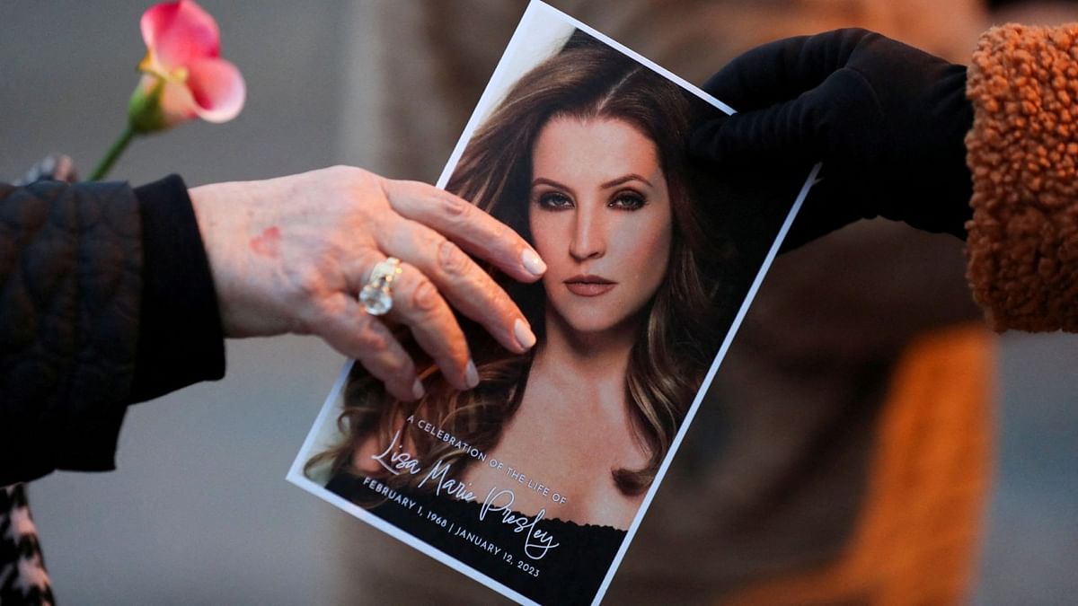 A music fan hands a picture of Lisa Marie Presley to another fan as they attend a public memorial for her. Credit: Reuters Photo