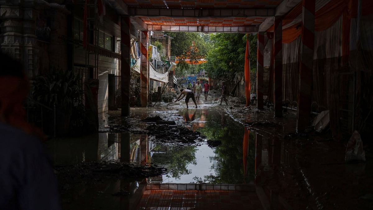 People clean the mud outside their house as the flood water recedes in New Delhi. Credit: Reuters Photo