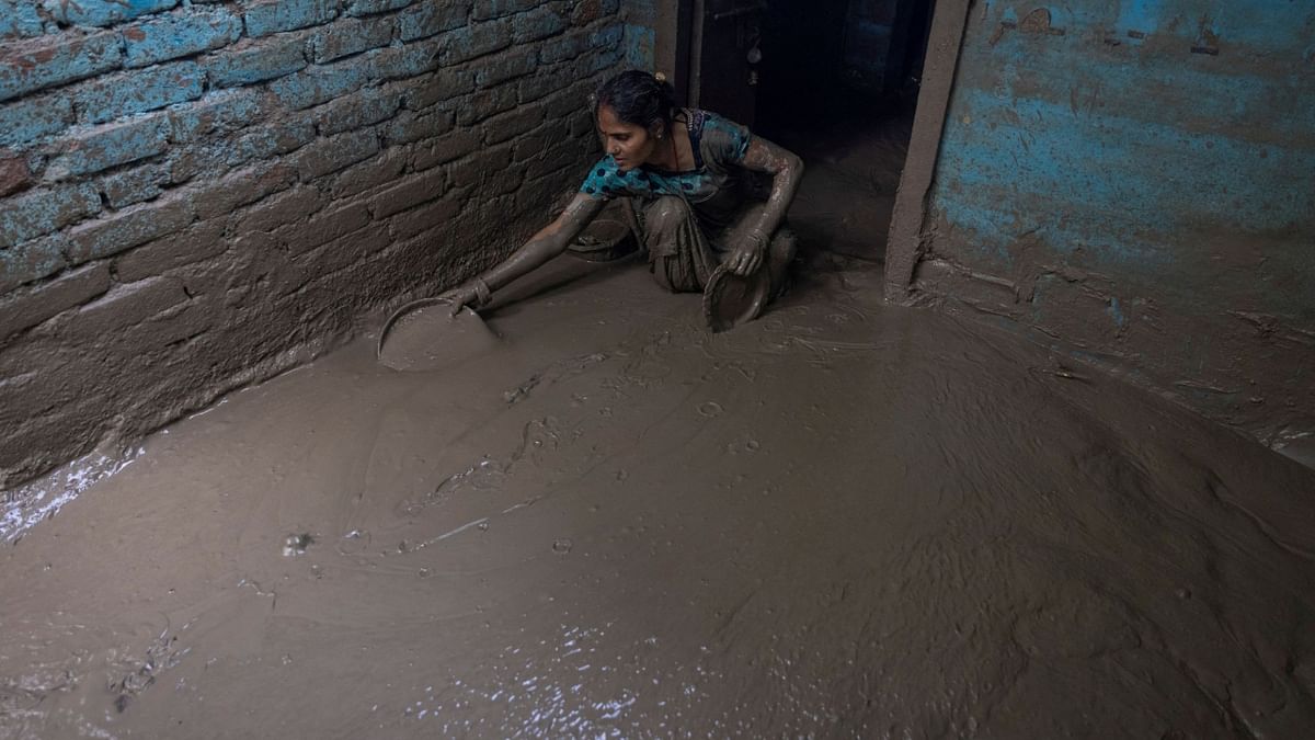 A woman cleans the mud from the entrance of her house as flood water recedes in Delhi. Credit: Reuters Photo