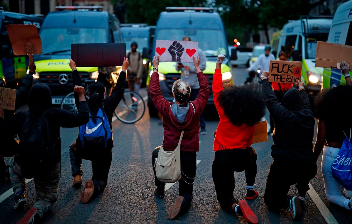 Protestors hold placards as they kneel in front of Police vans in Parliament Square, during an anti-racism demonstration in London. Credit: AFP Photo
