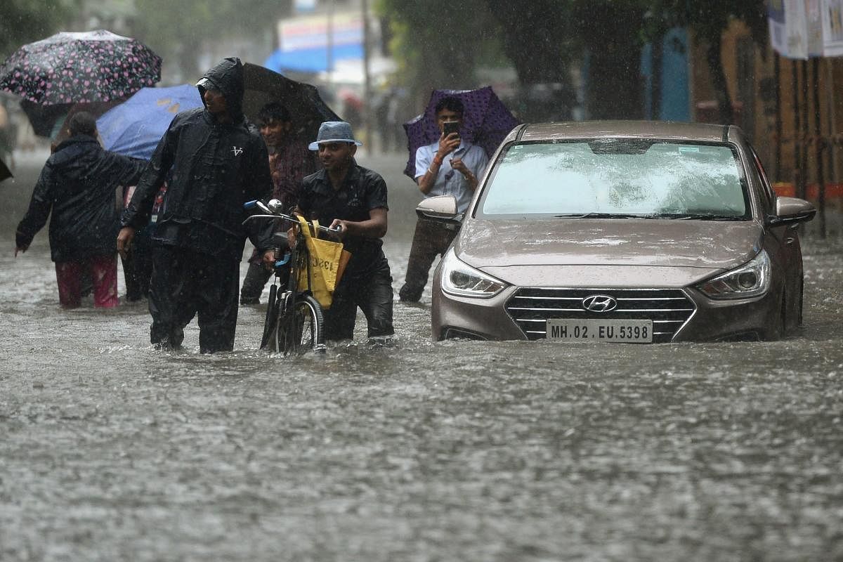 People walk on a flooded road during heavy rain showers in Mumbai. AFP File Photo