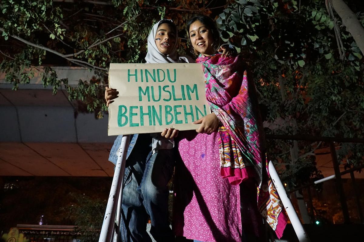 Two students from Srishti - Jennifer (a Muslim) and Dharani (a Hindu), hold a placard promoting Hindu-Muslim unity during a candlelight vigil in Bangalore on December 24, 2019. DH PHOTO/AKHIL KADIDAL